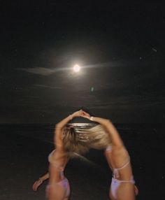 two women in bikinis are standing on the beach at night with their backs to each other