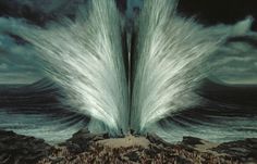 two large white waves crashing into each other in front of a dark sky with clouds