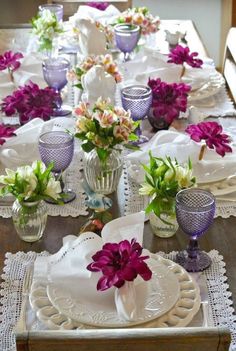 the table is set with purple and white flowers in glass vases, lace doily, and napkins