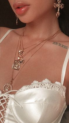 a woman with tattoos on her chest wearing a white dress and gold jewelry necklaces