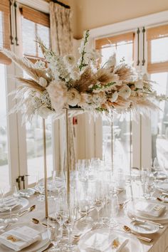 a tall vase filled with lots of flowers on top of a white table cloth covered table