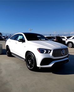 a white mercedes suv parked in a lot next to other cars on a sunny day