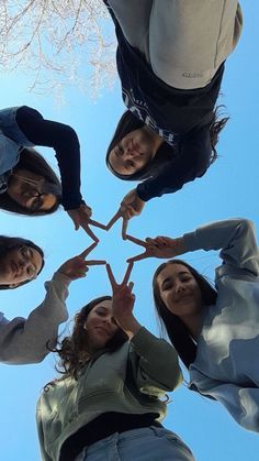 four people standing in a circle holding their hands together and making a heart with their fingers