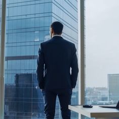 a man standing in front of a large window looking out at the cityscape