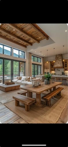 a large open living room and dining area with wood beams on the ceiling, windows overlooking mountains