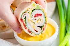 a person dipping some food into a small bowl with celery sticks in it