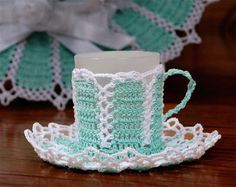 a crocheted tea cup and saucer on a wooden table next to a doily