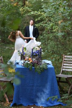 a bride and groom are standing in the woods near a table with candles on it