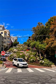 a white car driving down a street next to a lush green hillside covered in flowers