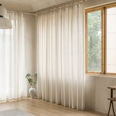 a living room with white curtains and a table in front of a window that has a potted plant on it