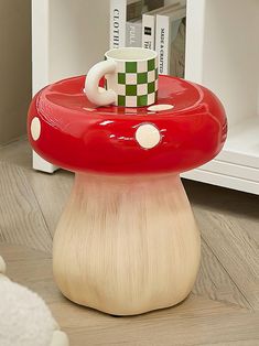 a mushroom shaped table with a coffee cup on it's top in front of a book shelf