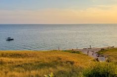 people are walking on the beach near the water and boats in the ocean at sunset