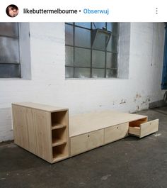 a wooden bench sitting in front of a window next to a white wall with windows