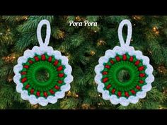 two crocheted christmas ornaments hanging from a pine tree with red berries on them