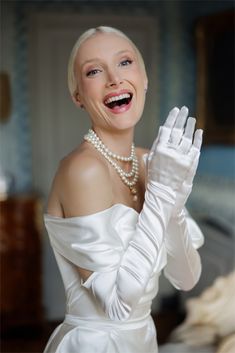 a woman in a white dress is smiling and holding her hands up to the side