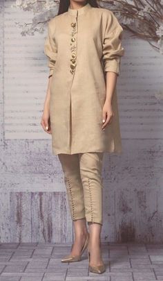 a woman standing in front of a wall wearing a tan outfit with buttons on the side