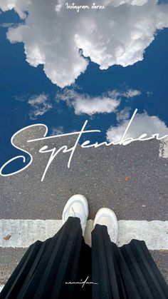 a person standing on the sidewalk with their feet in the air and clouds reflected in the water