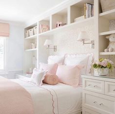 a white and pink bedroom with lots of shelves on the headboard, bedding and pillows