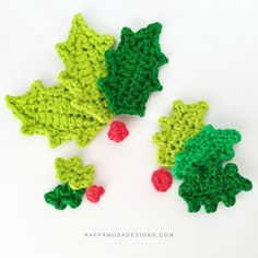 three crocheted holly leaves are shown on a white surface, one is green and the other is red