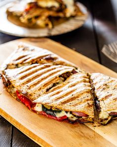 a cut in half sandwich sitting on top of a wooden cutting board next to another plate