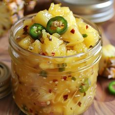 a jar filled with macaroni and cheese on top of a wooden table next to green peppers