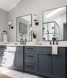 a bathroom with double sinks and mirrors on the wall, along with two vases filled with flowers