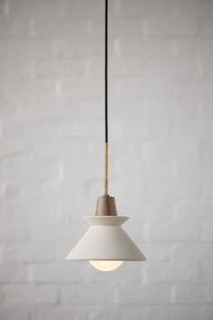 a white light hanging from a ceiling in front of a brick wall with a black cord