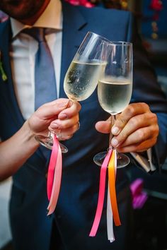 two people holding up wine glasses with ribbons on the handles, and one person wearing a blue suit