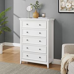 a white dresser sitting in a living room next to a chair and potted plant