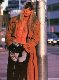 a man standing next to a pole on the side of a street with his shirt off