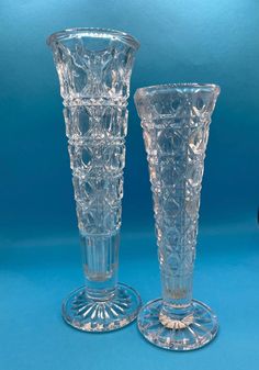 two clear glass vases sitting next to each other on a blue tablecloth background