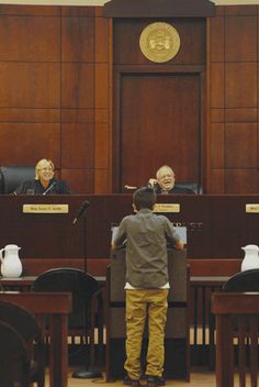 three people sitting at desks in front of a judge's bench with their backs to the camera