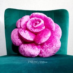 a large pink rose sitting on top of a green velvet chair with white walls behind it