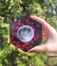 a person holding up a small piece of paper with the moon in it's center