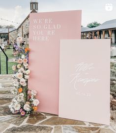 a pink wedding sign with flowers on it and the words we're so glad you're here