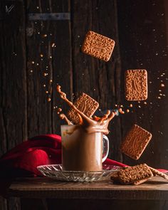 some cookies and milk are falling into a mug with chocolate on the table next to it