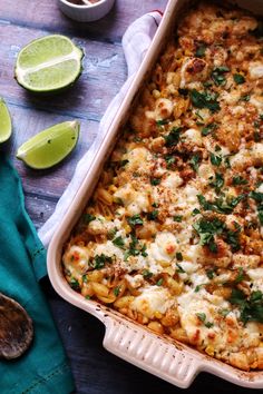 a casserole dish with cheese, meat and vegetables in it next to lime wedges