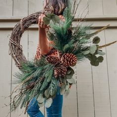 a woman holding a wreath with pine cones and greenery