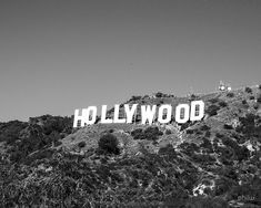 black and white photograph of hollywood sign on the side of a hill with trees around it