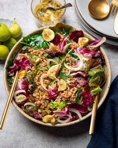 a bowl filled with salad next to two spoons and some other food on the table