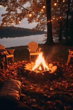 two adiron chairs sitting in front of a campfire with lights strung over it