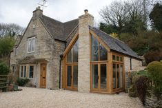 a stone house with wooden doors and windows on gravel ground in front of brick building