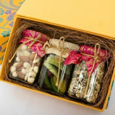 four jars filled with different types of nuts in a yellow gift box on a table