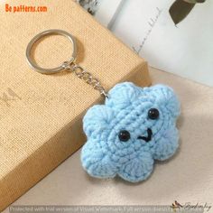 a blue crocheted keychain with a smiling cloud on it's face