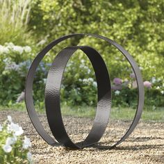 two metal rings sitting in the middle of a gravel road next to flowers and trees