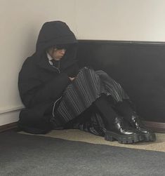 a person sitting on the floor in front of a wall with their legs crossed and wearing black boots