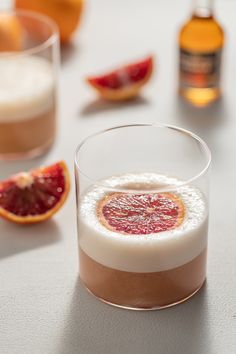 a glass filled with liquid sitting on top of a table next to sliced oranges