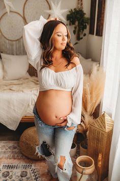 a pregnant woman standing in front of a bed wearing ripped jeans and a white top