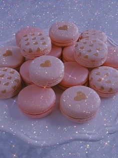 pink macaroons with gold hearts are on a white cloth covered tablecloth, surrounded by sparkles