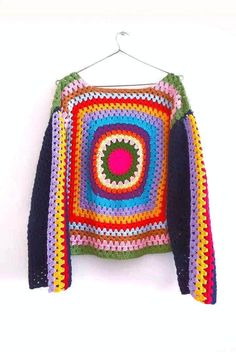 a colorful crocheted sweater hanging on a white wall